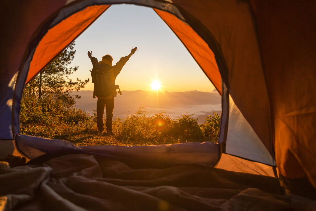 hiker levantar em a acampamento frente laranja barraca e mochila em a montanhas